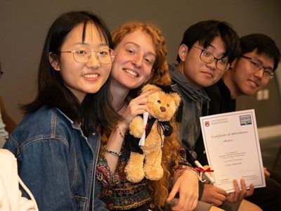 Summer School students at their awards ceremony holding a certificate and a teddy with mini graduation cap and gown